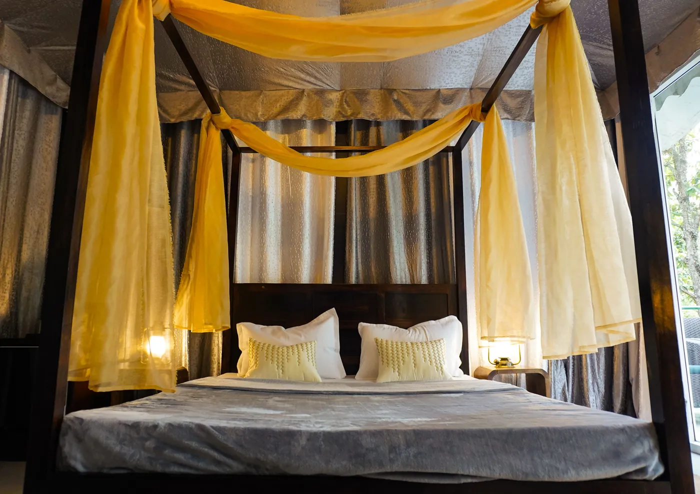 Elegant four poster bed with flowing yellow curtains in a cozy, serene bedroom setting.