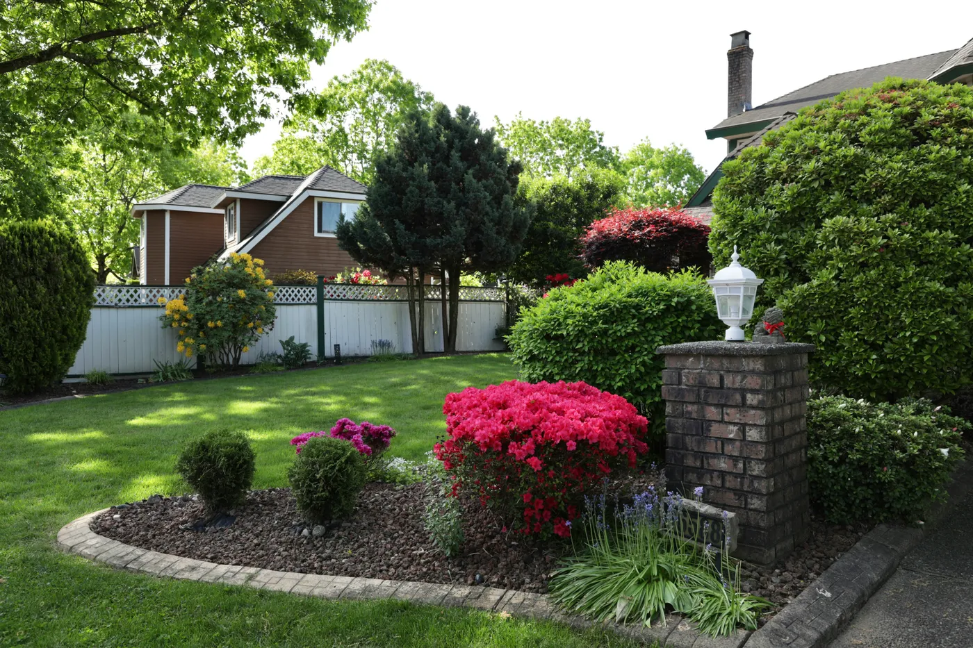 Lush green garden with blooming flowers and brick lamp post