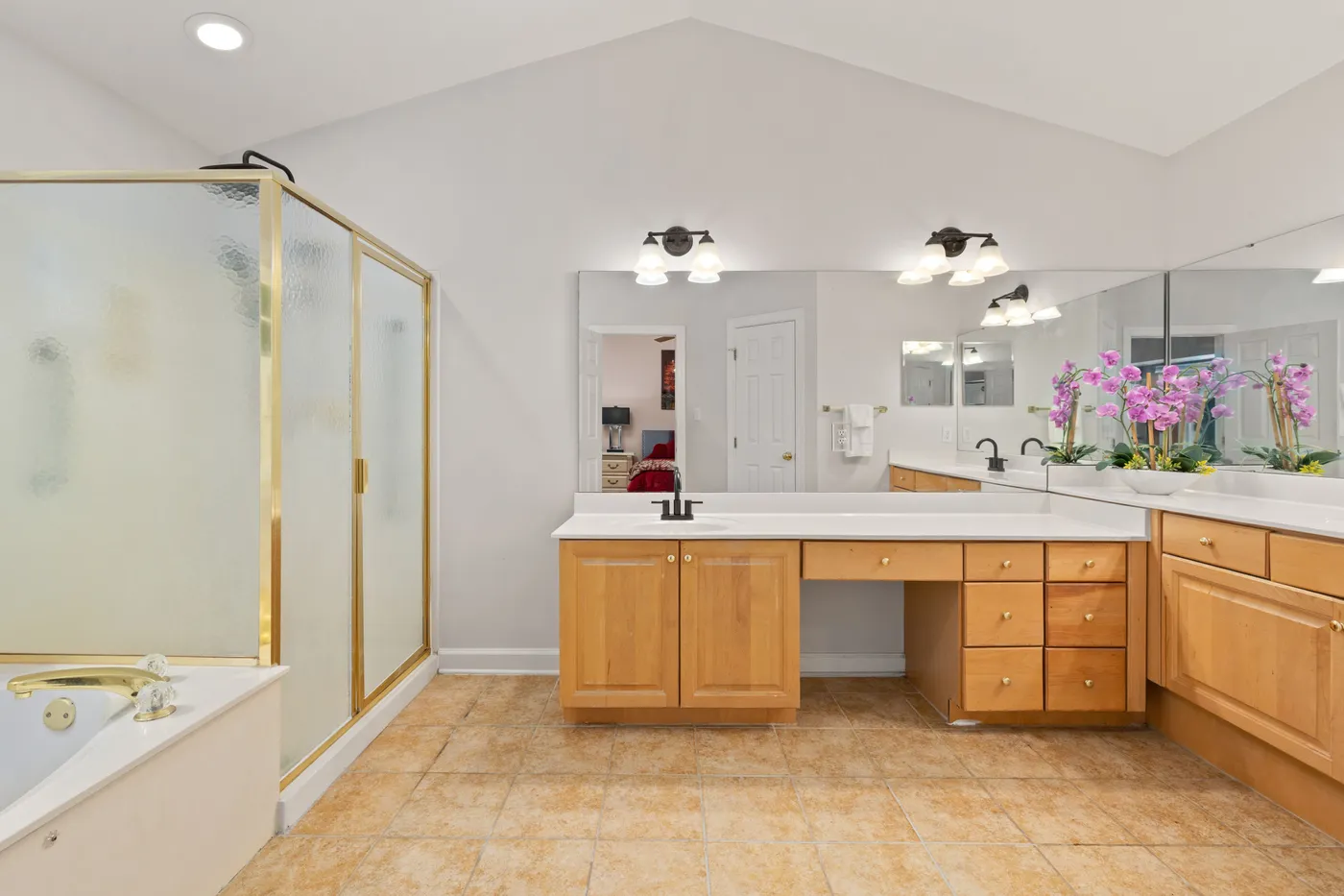 Spacious bathroom featuring wooden cabinets, large mirrors, and vibrant orchids.