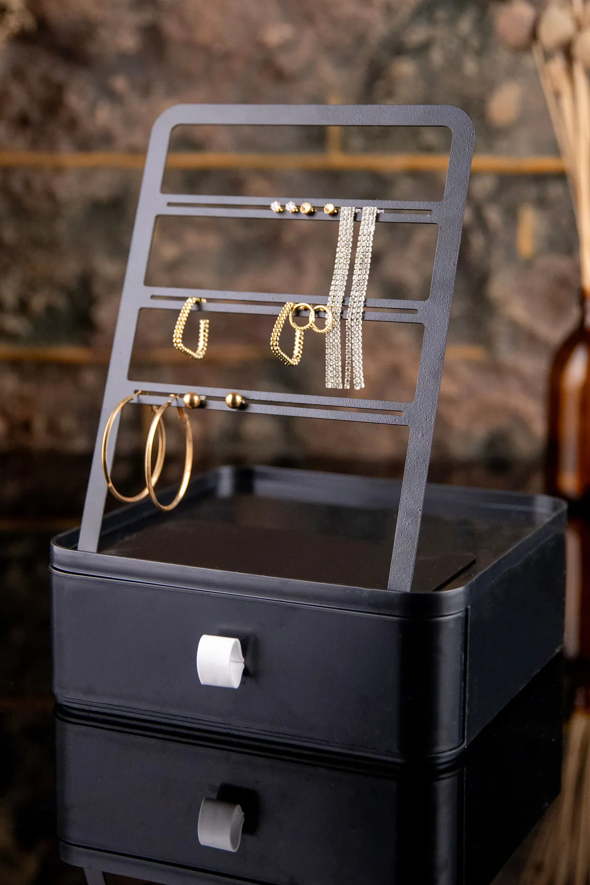 Stylish black jewelry stand showcasing elegant gold and silver earrings indoors.
