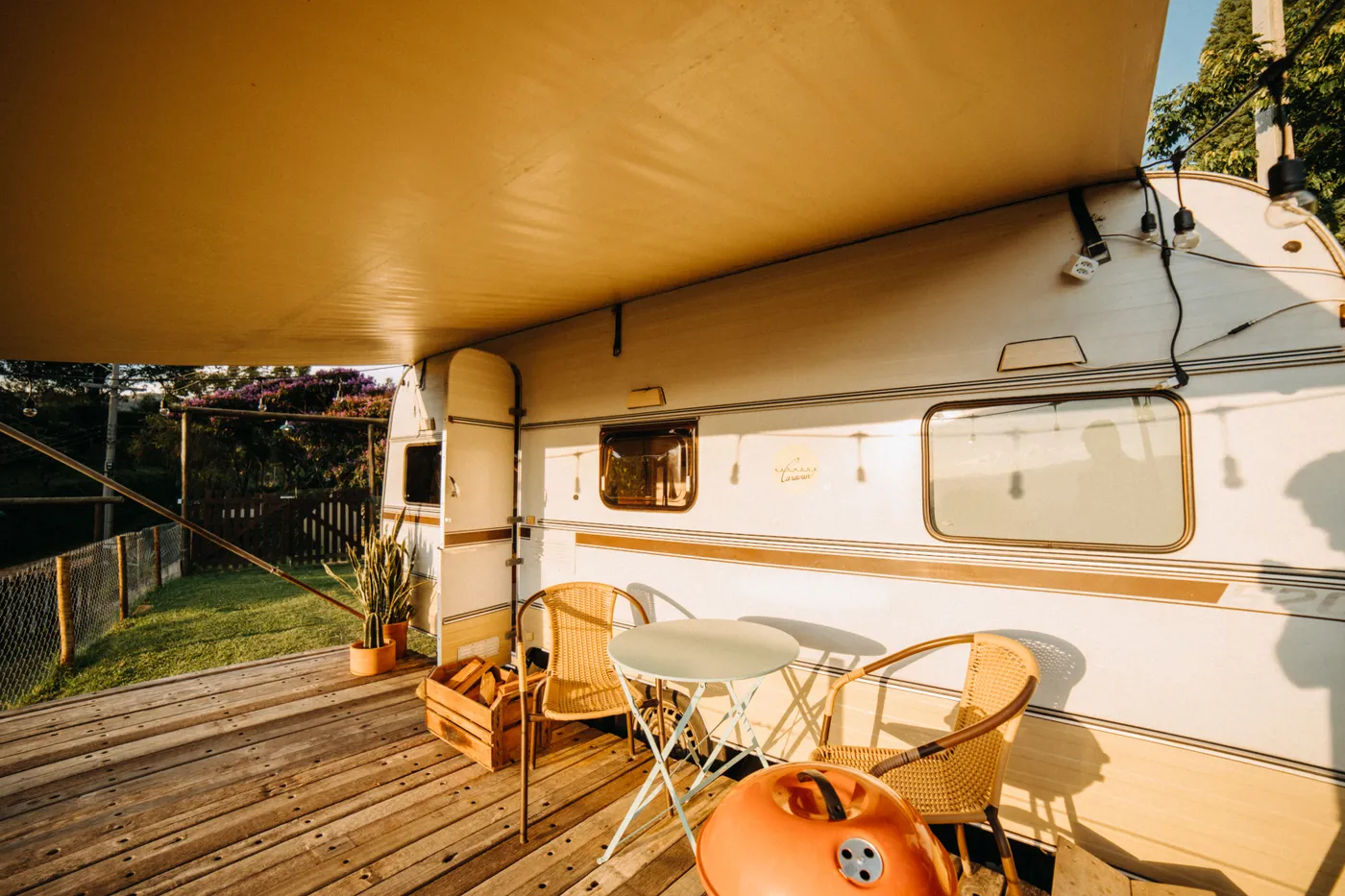 Sunlit caravan setup on a wooden deck with chairs and a canopy, perfect for summer camping.
