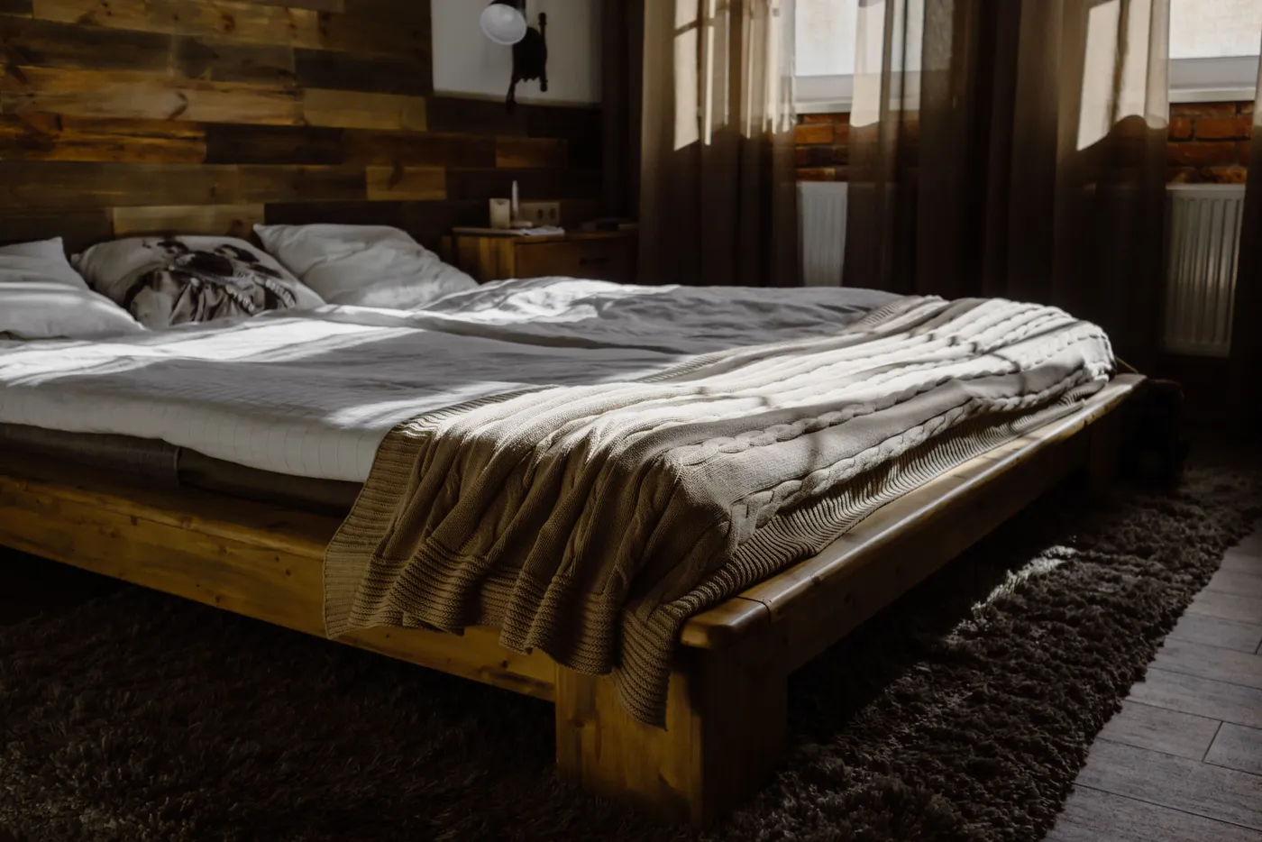 Sunlit modern bedroom with wooden bed frame and cozy blankets, offering interior design inspiration.