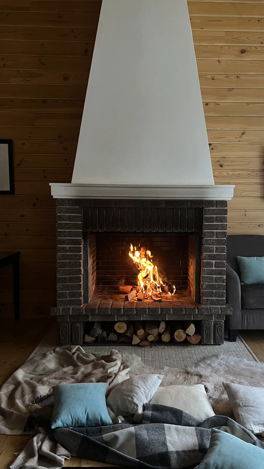 Warm living room with a lit fireplace, blankets, and pillows, perfect for relaxation.